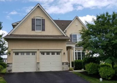 A large house with two garage doors and a tree.