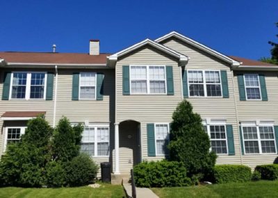 A house with green shutters and bushes in front of it.