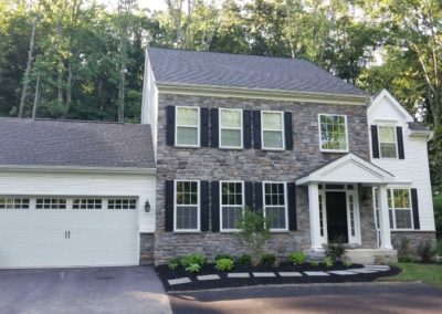 A large brick house with two garages and trees in the background.