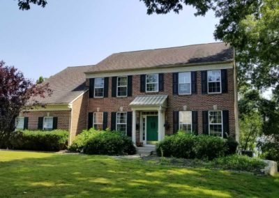 A large brick house with black shutters and green door.