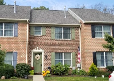 A brick house with green shutters and a flag.