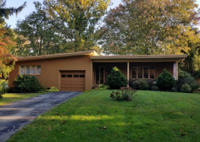 A brown house with a driveway and trees in the background.